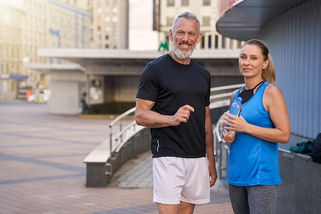 Joyful sportive middle aged couple man and woman in sportswear looking at camera standing together