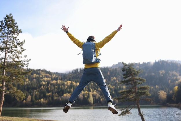 Joyful tourist with rucksack jumps on tranquil river bank