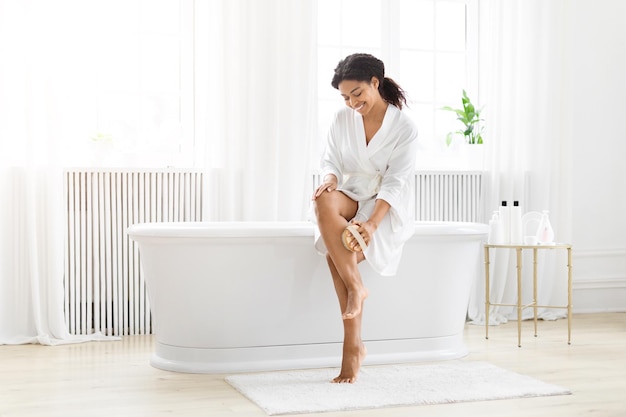 Joyful woman sitting on white bathtub massaging her legs