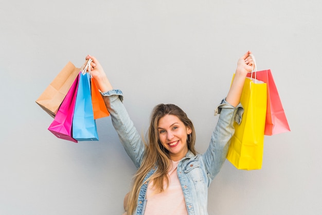 Joyful woman standing with shopping bags at light wall