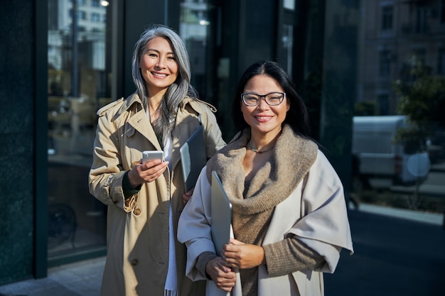 Joyful women with notebooks standing on the street