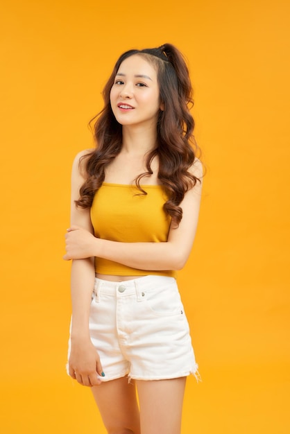 Joyful young asian woman in yellow crop top posing isolated on yellow background