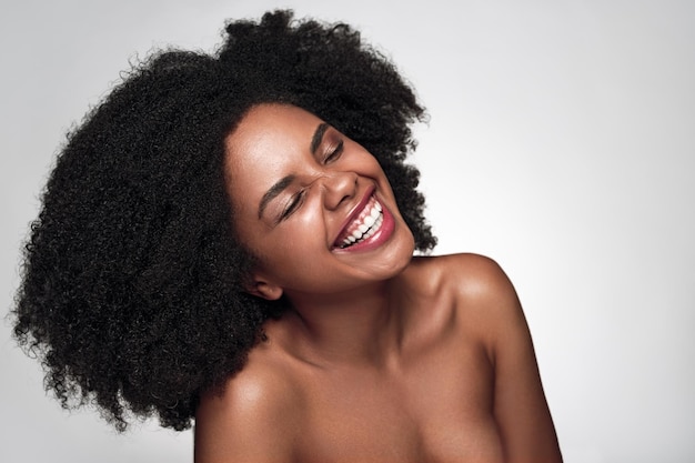 Joyful young black lady with perfect skin smiling with closed eyes