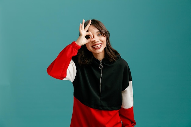 Joyful young caucasian woman looking at camera making peephole gesture isolated on blue background