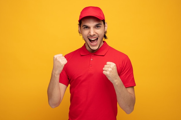 joyful young delivery man wearing uniform and cap looking at camera showing yes gesture isolated on yellow background