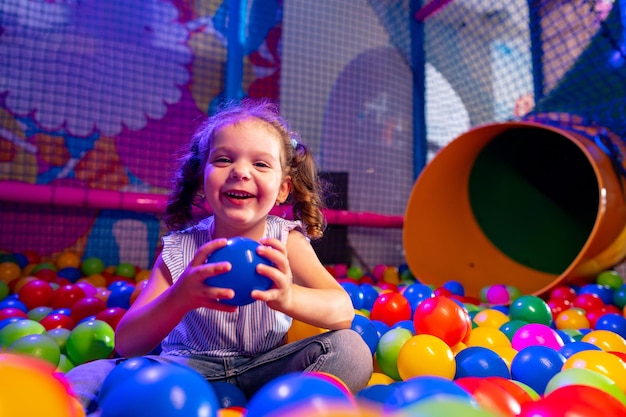 Joyful young girl playing in a colorful ball pit at an indoor playground