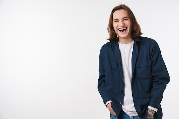 joyful young man with long hair laughing and looking at front isolated over white wall