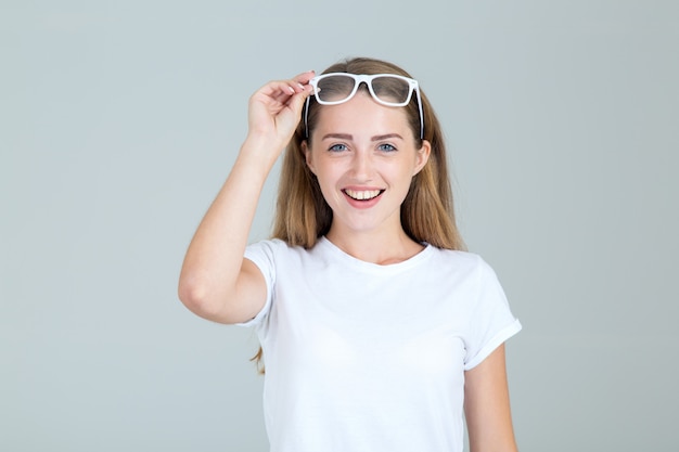 Joyful young woman raised her glasses over her head, isolated on gray