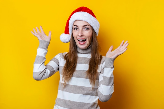 Joyful young woman in Santa Claus hat on a yellow background.