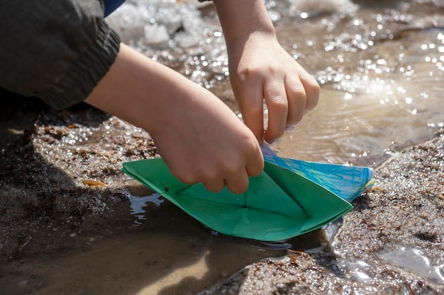 Joyfull Child boy of 67 year old in rubber boots playing with origami paper boats in muddy puddle Carefree childhood happy time