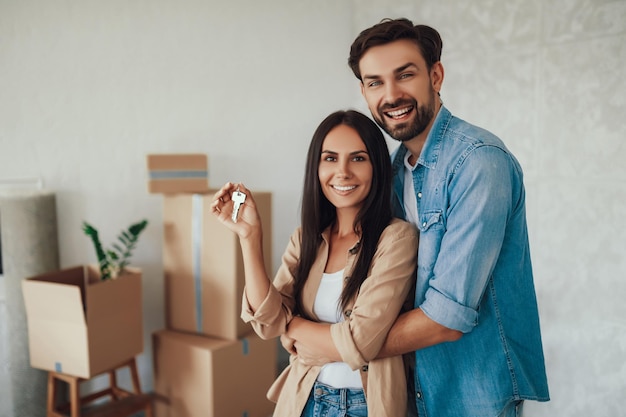 Joyous brunette lady holding keys to a new flat while being hugged by her loving husband