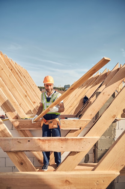 Joyous construction site worker holding a long piece of wood while building a roof frame