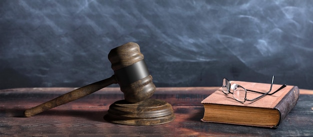 Judge gavel old books and reading glasses on a wooden table black board background 3d illustration