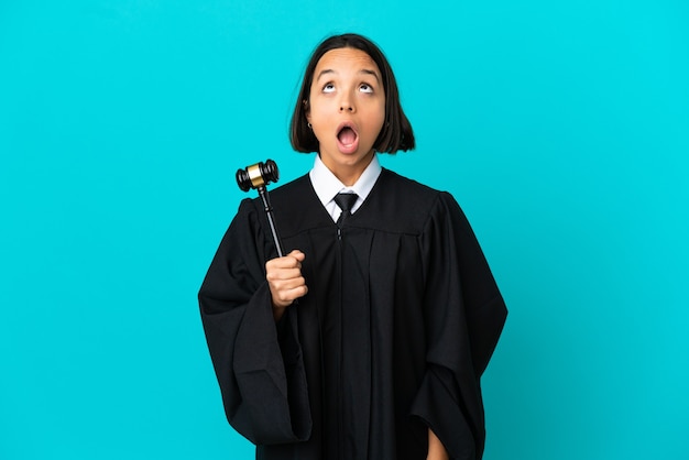 Judge over isolated blue background looking up and with surprised expression