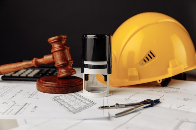 Judge wooden gavel, stamp and yellow helmet with construction plans.