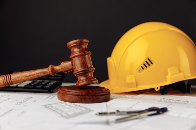 Judge wooden gavel and yellow helmet with construction plans.