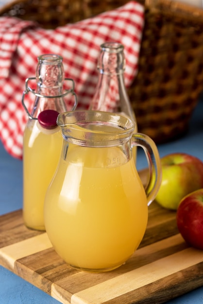 Jug and Bottle of Apple Juice with Pulp on Wooden Tray Blue Background Vertical