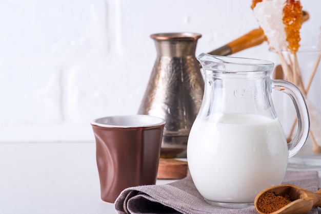 Jug of milk and ground coffee for making a drink at home on a stone countertop against a white kitchen wall