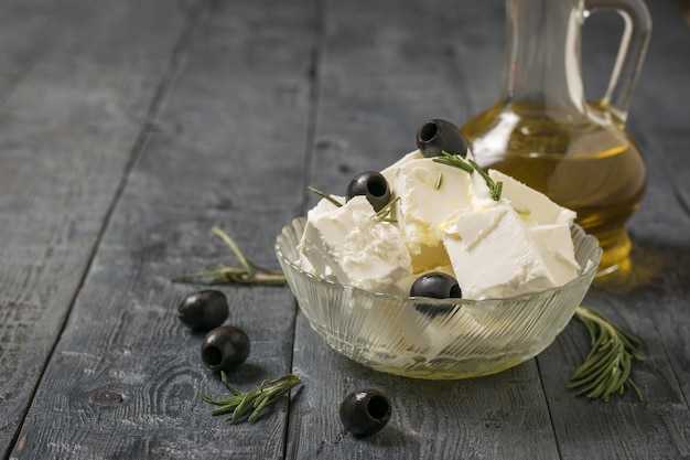 Photo a jug of olive oil and feta cheese with olives on a wooden table. natural cheese made from sheep's milk.