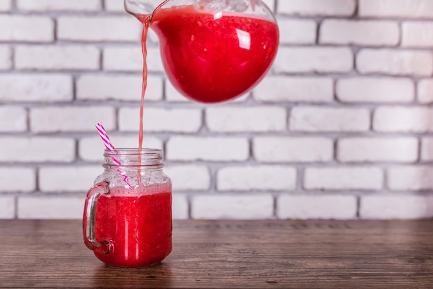 A jug pouring freshly blended red fruit smoothie in glass jar with straw selective focus harvest con