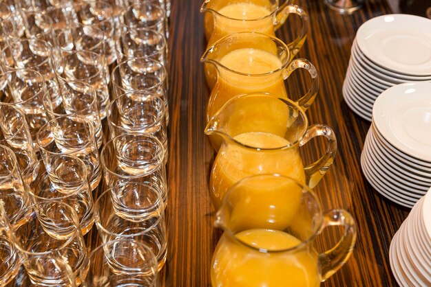 Jugs of orange juice rows of empty glasses and stacks of plates on a buffet table Holidays and celebrations