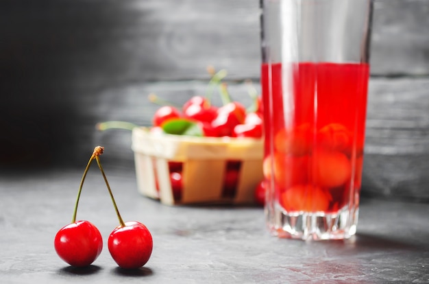 Juice or compote with cherries. fresh ripe red cherry in a basket on a gray concrete backg