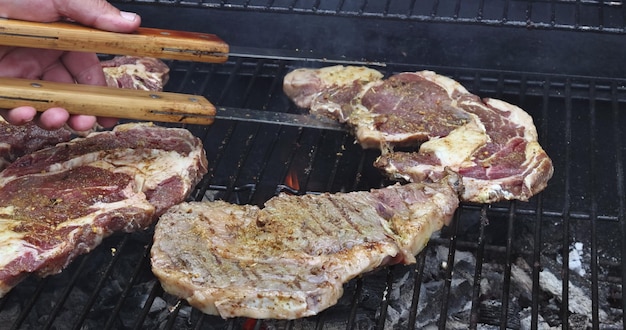 Juicy beef steak is grilled over fire of coals on an iron grill resulting in smokey flame that envel