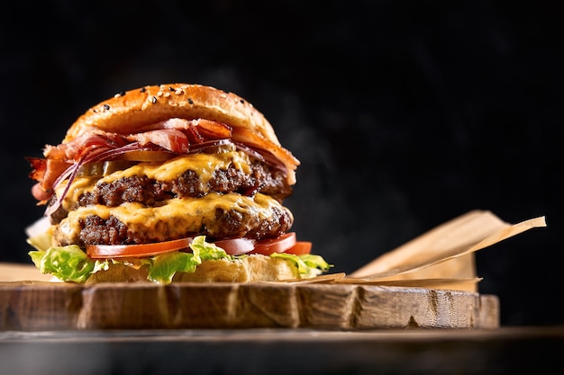 Juicy burger on the board, black background. Dark background, fast food. Traditional american food. Copy space.