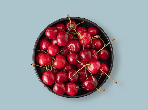 Juicy cherries in a black bowl on a blue background Top view and copy space