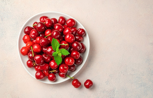 Juicy, delicious cherries and mint in a white plate on a pink background. Top view, copy space.