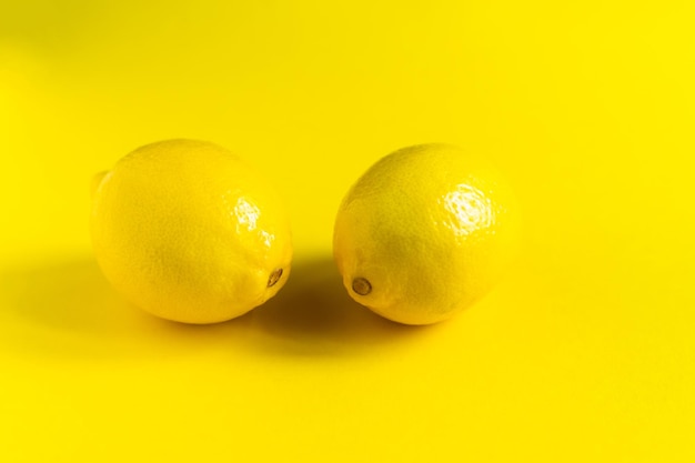 Juicy lemons on bright yellow background, citrus minimal concept. Flat lay, top view, copy space.