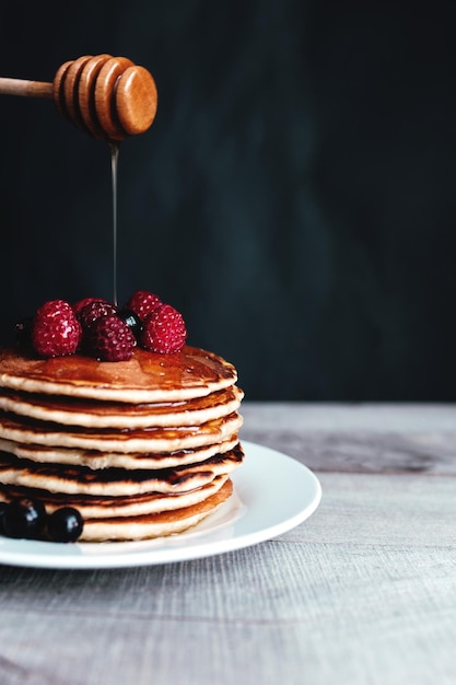 Photo juicy pancakes with berries and honey on a white plate spoon wooden table high quality photo