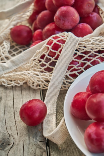 Juicy plums in eco friendly string eco mesh bag on a wooden background