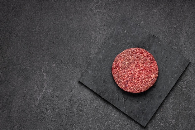 Photo juicy raw burger patty against a dark backdrop