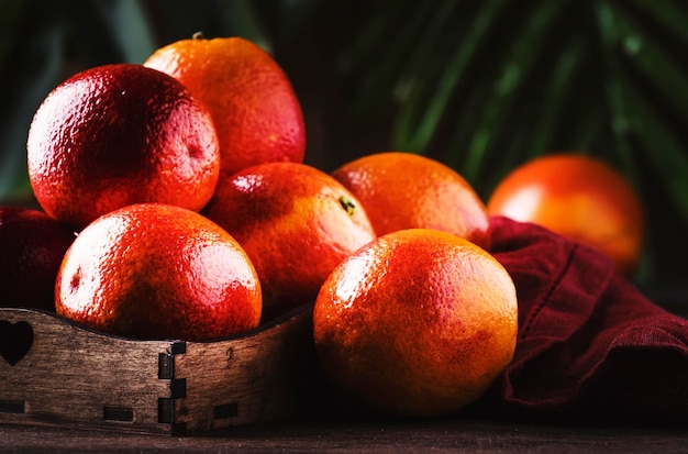 Juicy ripe shiny red bloody oranges in tray for making refreshing cocktail on rustic wooden table background still life selective focus