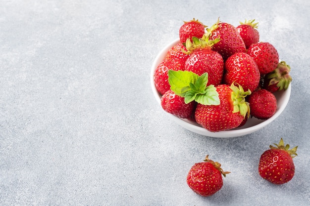 Juicy ripe strawberries in a plate on a concrete background. Sweet healthy dessert, vitamin harvest. copy space.