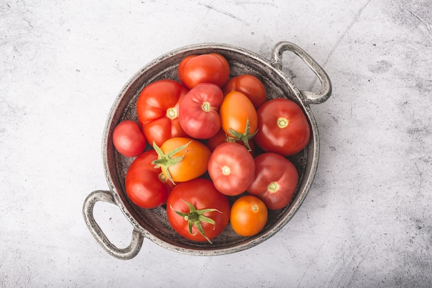 Juicy, ripe tomatoes in metal bowl with bunches on stone table