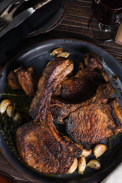 Juicy slice of fried pork chop on a bone in oil with garlic and herbs in a pan  Flat lay