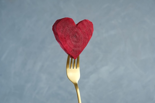 Juicy slice of raw beetroot in shape of heart on the tip of golden fork healthy eating raw food diet