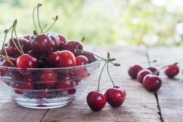 Photo juicy sweet cherries in a glass bowl closeup on wooden table with green bokeh background summer frui