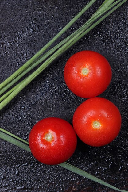 Juicy sweet red tomatoes and green sprigs on a black background Healthy food concept Closeup