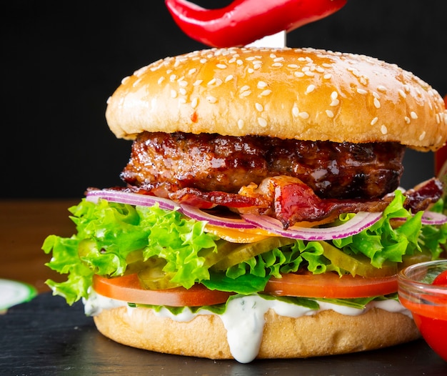 Juicy tasty burger with cheese, bacon and tomatoes. Cheeseburger close-up.