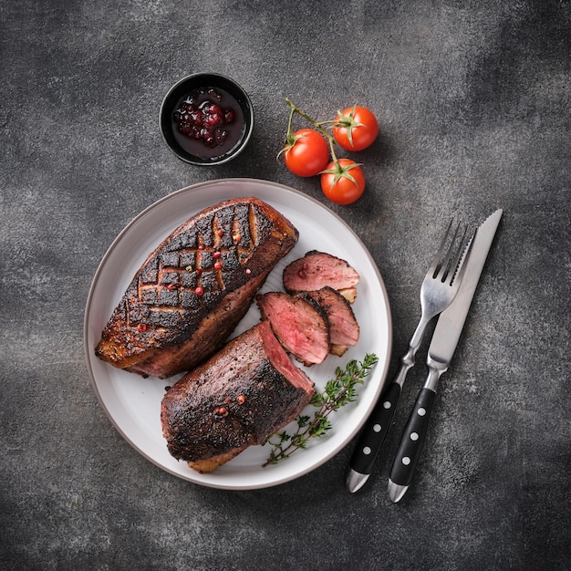 Juicy tasty fragrant roasted duck breast on a white plate with peppers and cherry tomatoes