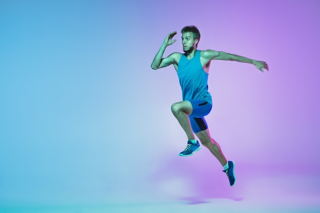 In jump Portrait of young caucasian man running jogging on gradient studio background