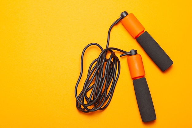 Jump rope. Fun exercises for body health. Orange rope with black cord. Yellow orange background.