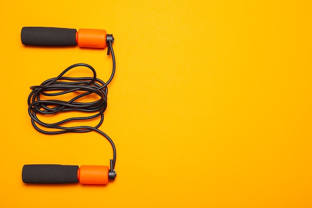 Jump rope. Fun exercises for body health. Orange rope with black cord. Yellow orange background.