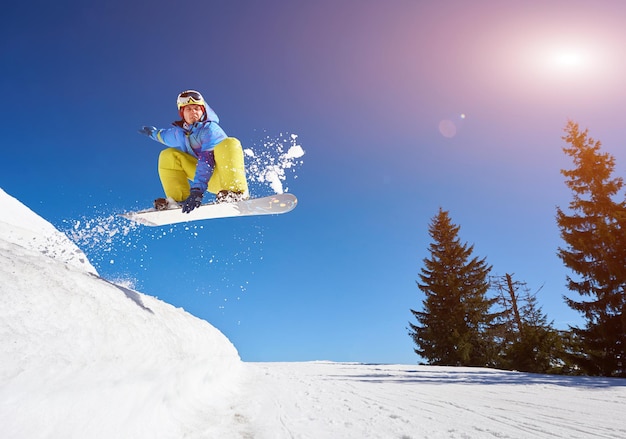 Jumping snowboarder keeps one hand on the snowboard on blue sky background