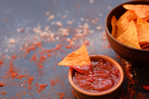 Junk fast food and unhealthy eating nacho tortilla chips in a bowl triangular crunchy slice dipped in salsa tomato sauce