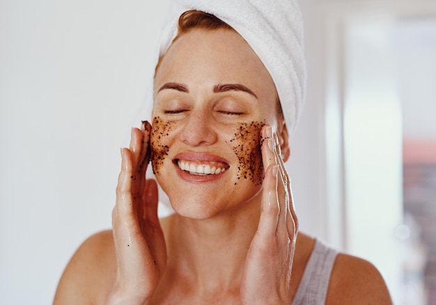 Just another way to show your face some love Cropped shot of an attractive young woman smiling while applying a coffee mask on her face at home