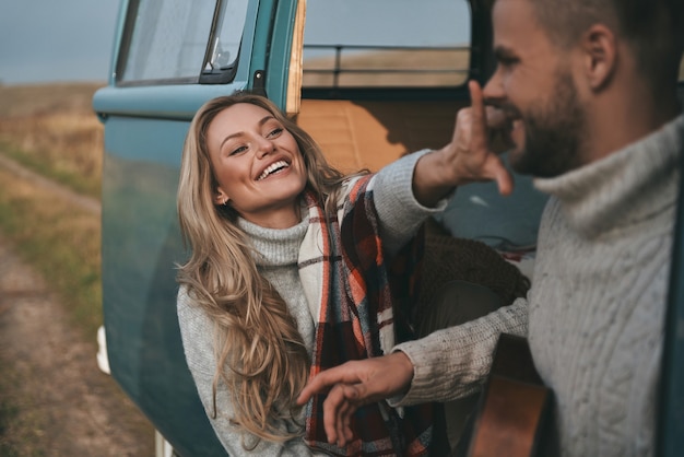 Just having fun. Beautiful young woman touching her boyfriend nose and smiling while sitting near the retro style mini van